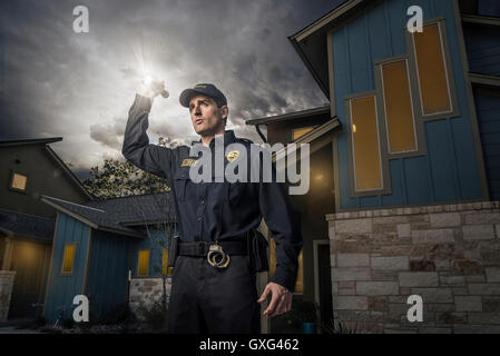 Caucasian police officer shining flashlight near house Stock Photo