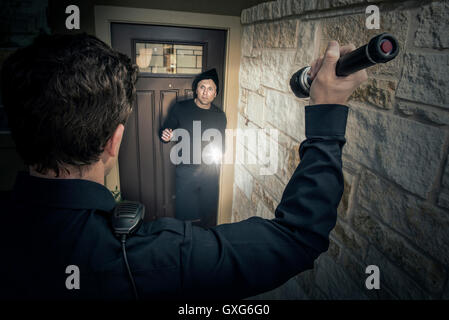 Caucasian police officer shining flashlight on house burglar Stock Photo