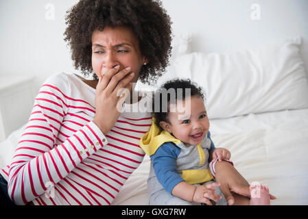 Mother yawning on bed holding baby son Stock Photo