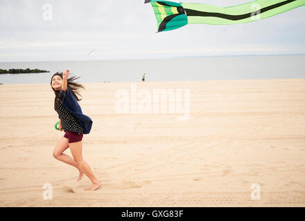 Mixed Race woman running on beach flying kite Stock Photo