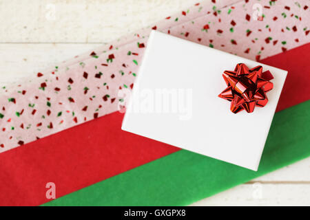 Small white gift box with red bow on colorful red and green tissue paper. Stock Photo