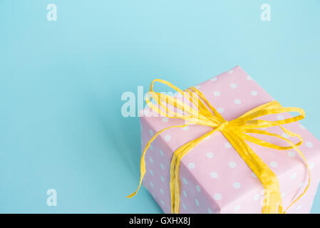 Top view of a gift box wrapped in pink dotted paper and tied yellow bow over light blue background. Stock Photo