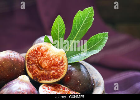 Fresh ripe black figs and fig leaf in rustic bowl on purple background. Copy space Stock Photo
