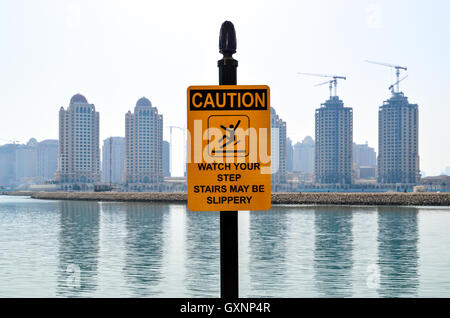 Caution sign in Doha, Qatar, with cranes building new residential towers Stock Photo