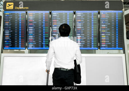 Business travel concept - Asian young business man with luggage waiting for travel in airport near flight timetable. Stock Photo