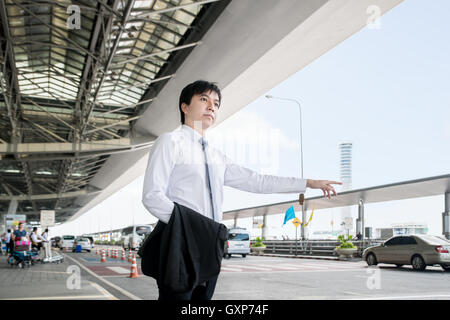 Business travel concept - Young Asian business man calling taxi at the airport. Stock Photo