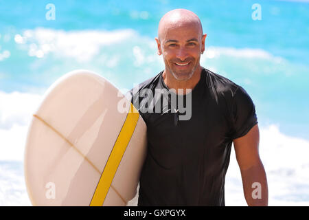 Portrait of a handsome man with surf board in hand, beautiful surf trainer on the beach, enjoying water sport, active summer Stock Photo
