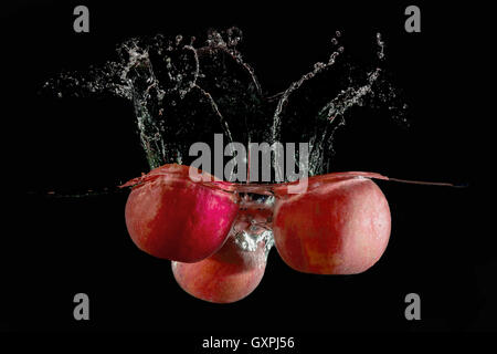 red apples fell into the water and climb up many splashes on black background Stock Photo