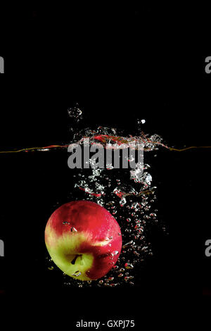 red apple fell into the water and climb up many splashes on black background Stock Photo