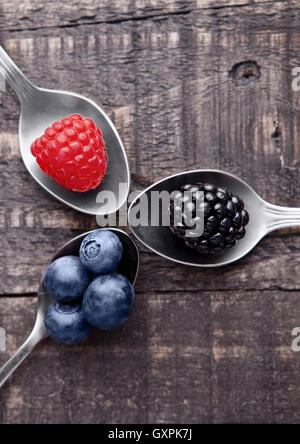 Raspberry blueberry and blackberry on spoon and wooden table. Still life photography Stock Photo