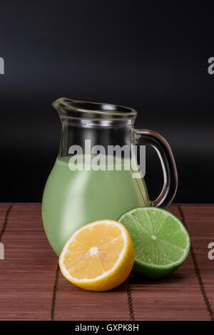 lime, lemon and pitcher of juice on bamboo mat on a dark background Stock Photo