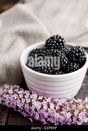 Blackberry in white bowl and flowers on wooden background. Natural healthy food.Still life photography Stock Photo