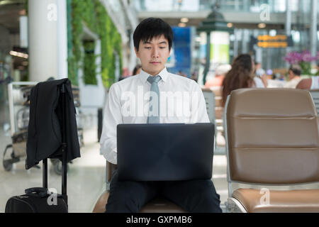 Asian young business traveler using laptop computer in airport lounge while waiting flight at airport. Business travel concept. Stock Photo