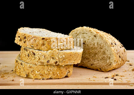 Sliced granary baguette on chopping board, against a black background Stock Photo