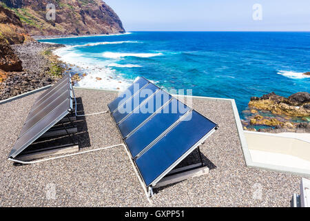 Rows of blue solar panels on house near beach, ocean and mountain Stock Photo
