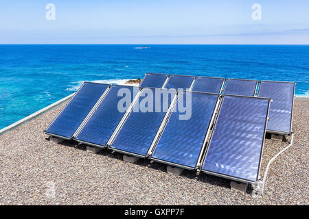 Group of blue solar panels on roof near water of ocean Stock Photo