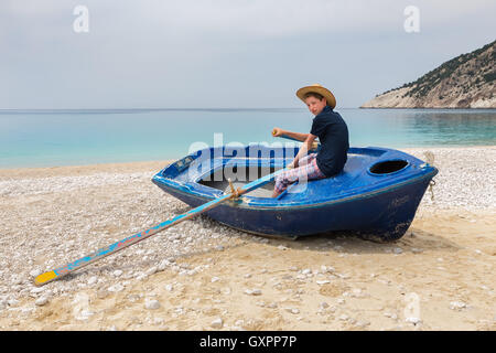 Dutch teenage boy rowing in blue boat on greek beach Stock Photo