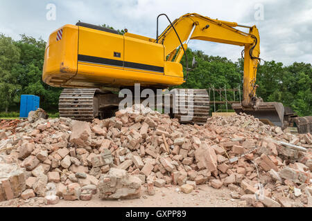Yellow belt excavator on heap of bricks of demolished house Stock Photo
