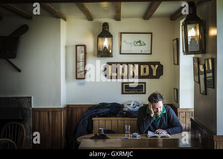 A man sits reading his book, illuminated by the light from a window, in the Marisco Tavern on Island. Stock Photo