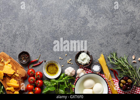 Italian food ingredients background with raw spaghetti, different kinds of cheese, olives, basil leaves, rosemary, garlic, chili Stock Photo