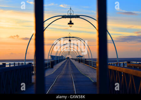 Old tram lines on Southport pier in Liverpool at sunset with old fashioned lanterns from behind railings Stock Photo