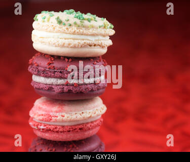Stack of Christmas macarons: vanilla and basil, candycane and mulled wine flavors, on a red tablecloth