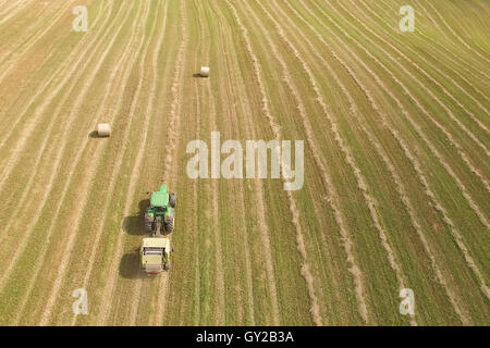 Aerial view of tractor with round baler rolling bales of straw on harvested field Stock Photo