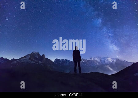 Person watching the stars and the Milky Way in the night sky above the Alps mountain range and the White Mount near Chamonix Stock Photo