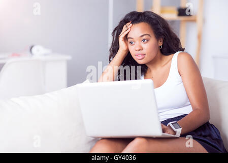 Thoughtful young woman sitting on the couch Stock Photo