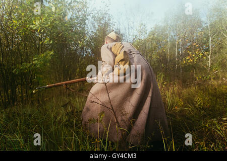 Unidentified re-enactor dressed as Soviet russian soldier running with rifle in forest grass in fog Stock Photo