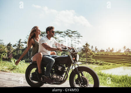 Side view shot of young couple on motorbike. Man riding on a motorcycle with girlfriend on country road. Stock Photo