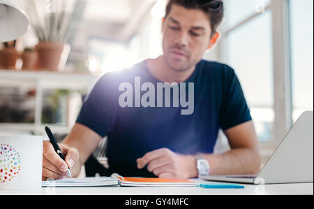 Shot of young man sitting at desk writing notes. Businessman working at his desk, with focus on hand. Stock Photo