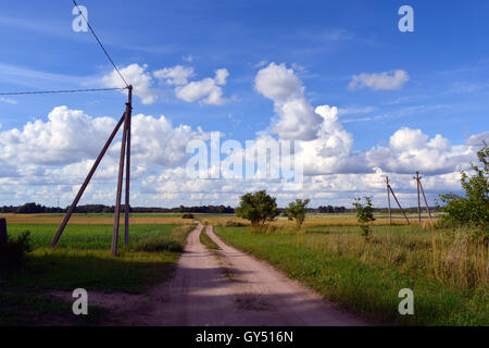 Unpaved country road through the fields on sunny cloudy summer day Stock Photo