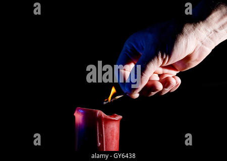 human hand with a match lights a red candle on the black background Stock Photo