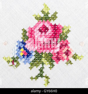Rose motif hand embroidery on white linen tablecloth.  Multicolored cross stich decoration with yarn. Handicraft. Macro photo. Stock Photo