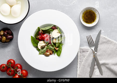 Italian salad with fresh basil leaves, olives, capers, walnuts, mozzarella cheese and red pepper on stone background. Stock Photo