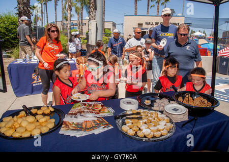 Multiracial athletic fan uniformed tween girls join adults at a dessert buffet line during half time at a college women's softball game in Fullerton, CA. Stock Photo