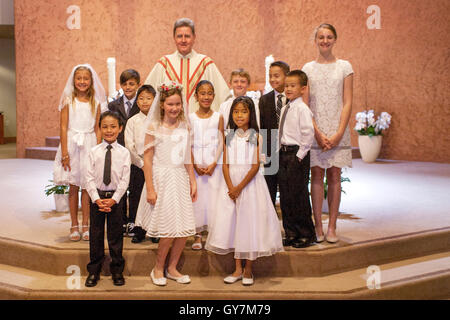 Formally dressed multiracial teens and tweens pose proudly with their monsignor at a Laguna Niguel, CA, Catholic church at the conclusion of their First Communion mass. First Communion is a ceremony in some Christian traditions during which a person first Stock Photo