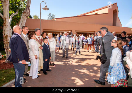A robed monsignor poses for photos with formally dressed multiracial teens and tweens in the courtyard of a Laguna Niguel, CA, Catholic church at the conclusion of their First Communion mass. First Communion is a ceremony in some Christian traditions duri Stock Photo
