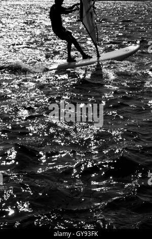 Black & White photograph of a windsurfer on windsurfing board on the sea,  the windsurfer is silhouetted against the back sunlig Stock Photo