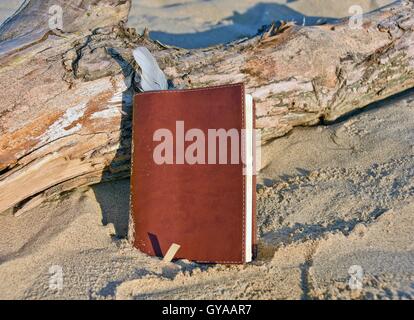 brown leather journal with white feather bookmark in sand Stock Photo