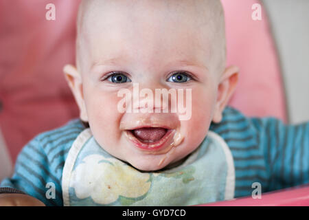 Beautiful baby eats porridge from mom's hand. He is sitting on a pink children' chair. Stock Photo