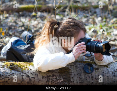 Portrait of photographer (young woman). The girl is hidding to take secretively images of wild life in a spring day sunny forest Stock Photo