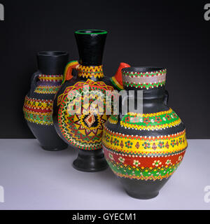Still life of three black decorated handcrafted pottery vases on background of white table and black wall Stock Photo