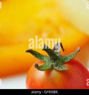 Tomato with green tail on the background of yellow pepper Stock Photo