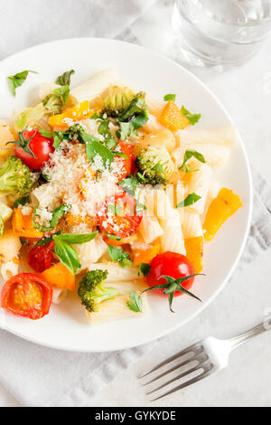 Italian pasta with vegetables (tomatoes, broccoli, pepper and greens) and parmesan cheese on white background - healthy vegetari Stock Photo