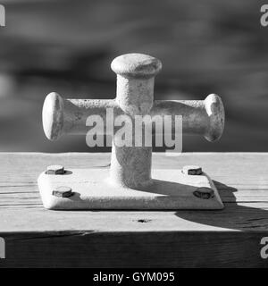 Small mooring bollard mounted on wooden pier, port equipment. Black and white photo Stock Photo