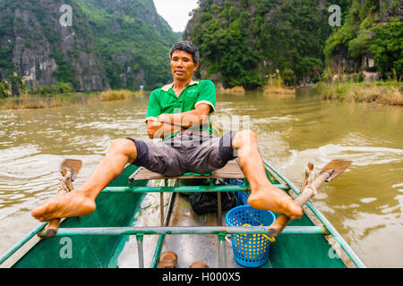 Local man rowing with his feet on the Ngo Dong River, Song Ngô Dong, Tam Coc, Ninh Binh, Vietnam Stock Photo