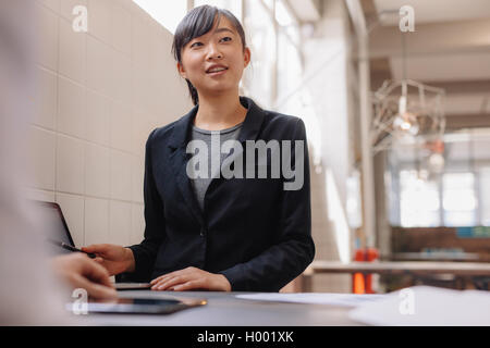 Shot of confident young Asian business woman giving presentation to coworkers in office. Stock Photo