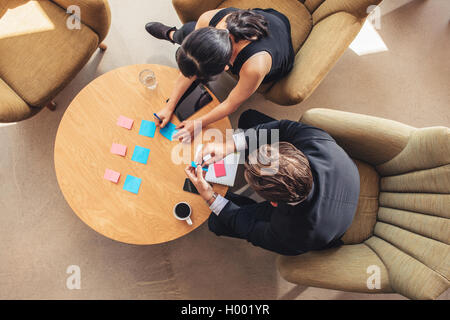 Top view of businessman and businesswoman discussing over adhesive notes on table in office lobby. Businesspeople preparing post Stock Photo